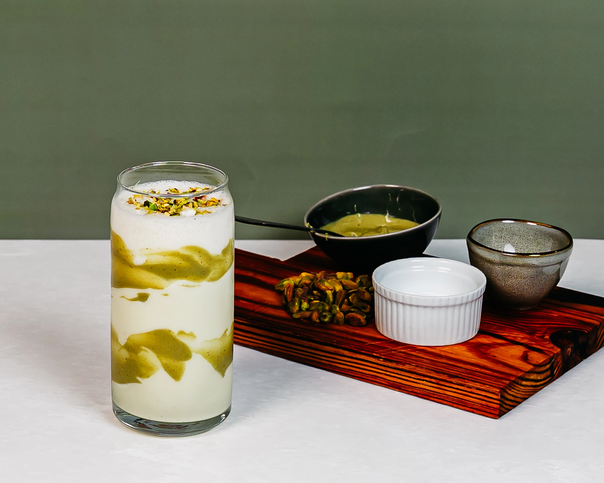 Pistachio White Chocolate shake with creamy pistachio sauce and topped with crushed pistachios, served beside pistachio ingredients.